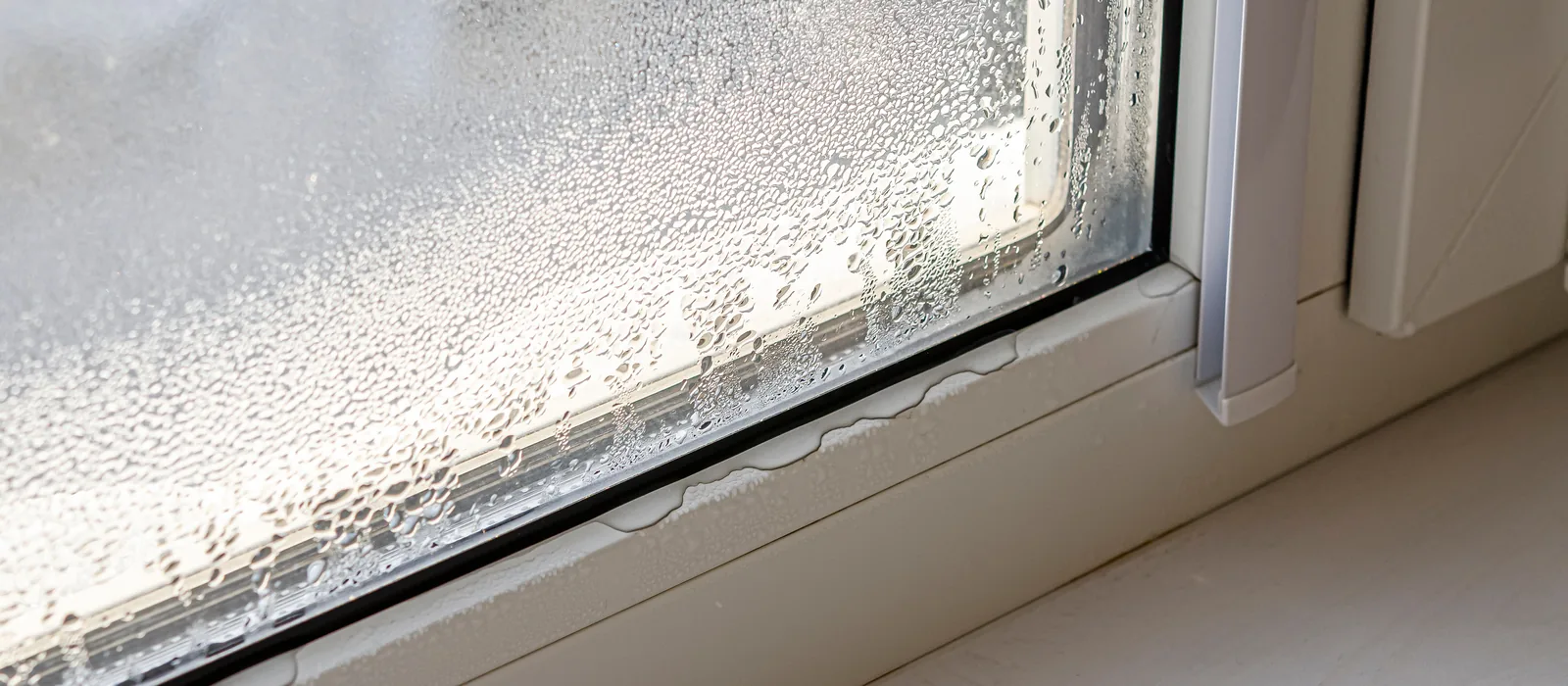 Heavy condensation running down the inside of a window pane onto the frame